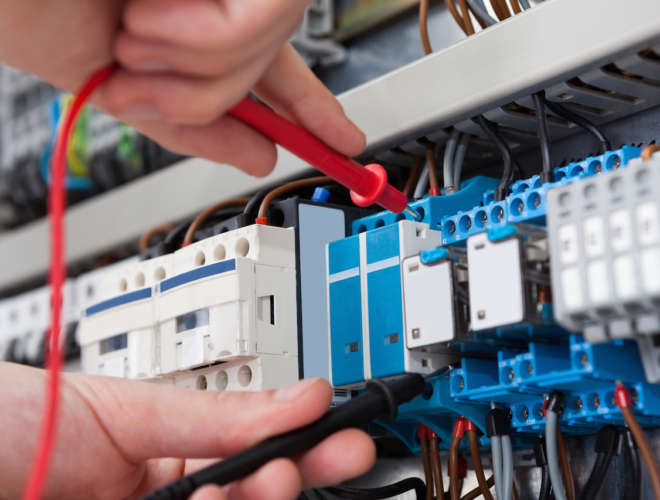 Closeup of male electrician examining fusebox with multimeter probe