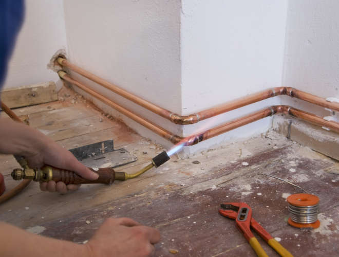 plumber soldering a copper pipe as part of aheating system
